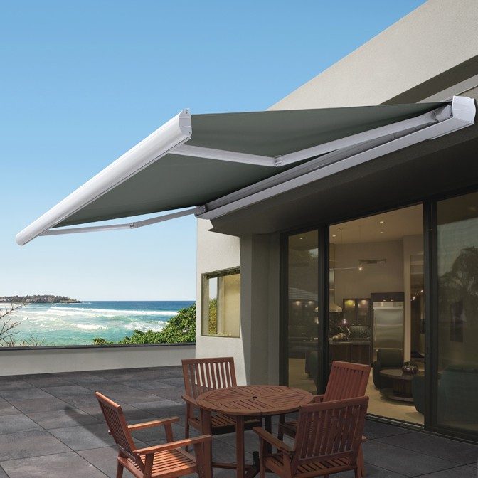Folding arm awning attached to house extended over deck table and chairs